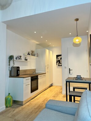 Una cocina moderna con armarios blancos, encimera de madera y horno empotrado. Hay una mesa de comedor con un banco y una lámpara colgante.