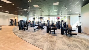 A spacious gym with various exercise machines, large windows, and a high ceiling.