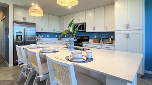 A modern kitchen with white cabinetry, a central island with bar stools, a refrigerator, microwave, and a toaster.