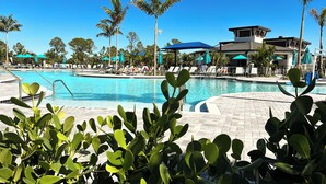 A pool area with lounge chairs and umbrellas, surrounded by palm trees and a building with a modern design.