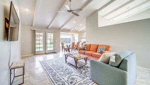 Een ruime woonkamer met een plafondventilator, een bank, een salontafel en een kamerbreed tapijt met een patroon.