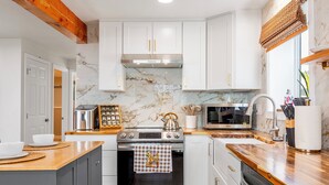 A modern kitchen with white cabinets, a stainless steel stove, and a wooden countertop.