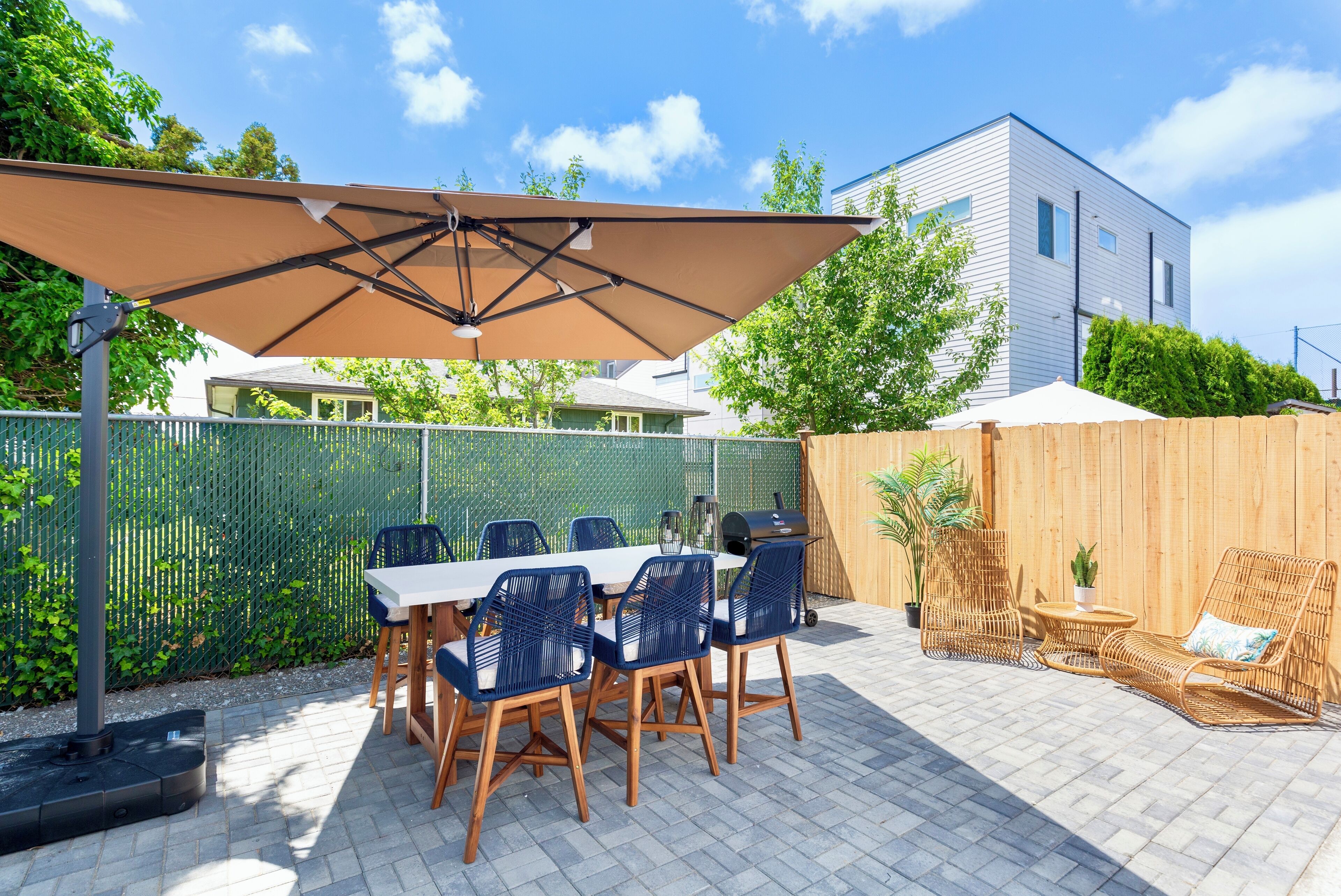 Een terras buiten met een tafel, stoelen, een barbecue en een grote parasol.