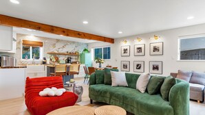 A modern living room with a green sofa, red chair, and wooden coffee table. A kitchen is visible in the background.