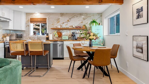 A modern kitchen with white cabinets, a wooden ceiling, and a dining area with brown chairs and a table.