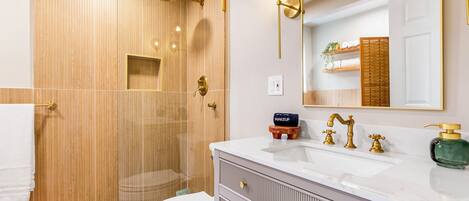 A modern bathroom with a wooden shower enclosure, a white sink with gold fixtures, and a large mirror.
