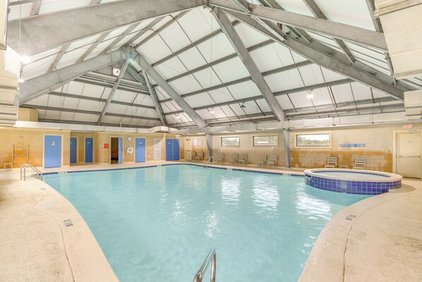 Una piscina interior con techo alto, un jacuzzi de azulejos azules y una fila de puertas azules.