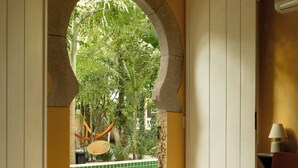 A bedroom with a large bed, an open archway leading to a balcony, and a view of greenery outside. - O Portalzinho (Paraty)