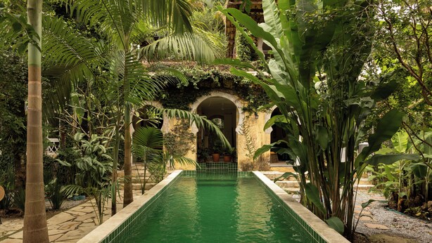 A pool with a tiled edge, surrounded by lush greenery and an archway. - O Portalzinho (Paraty)