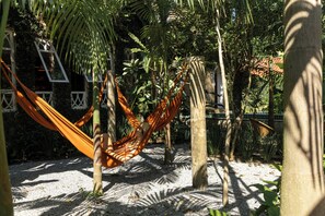 A hammock in a garden with a building in the background. - O Portalzinho (Paraty)