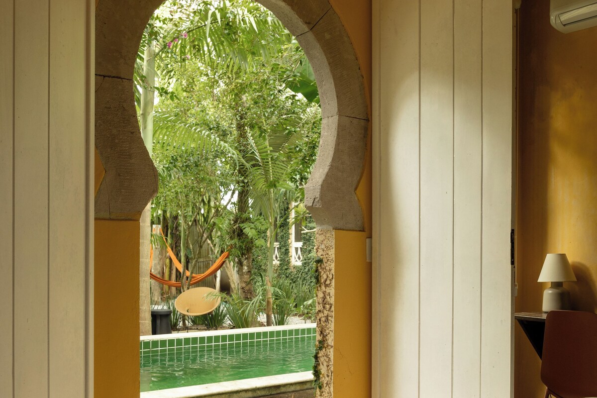 Un dormitorio con una cama grande, un arco abierto que da a un balcón y vistas a zonas verdes.