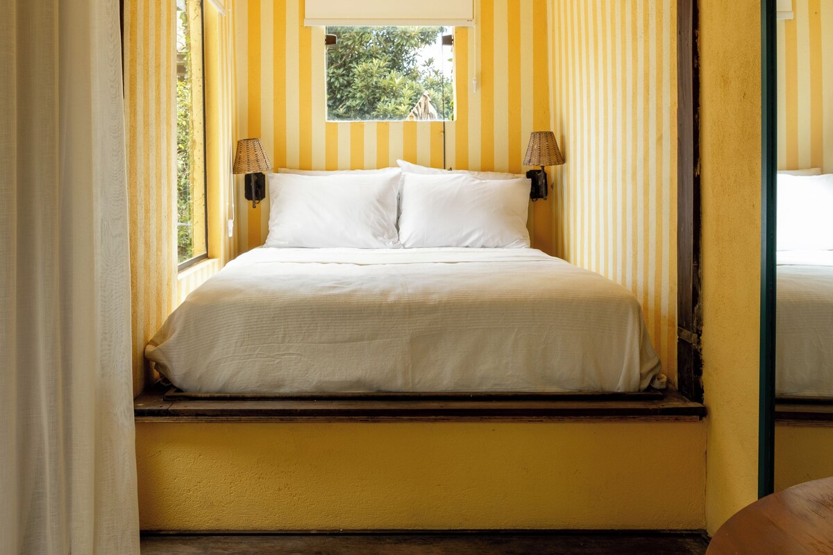 Un dormitorio con una cama, dos lámparas de noche, una ventana y vista a zonas verdes.