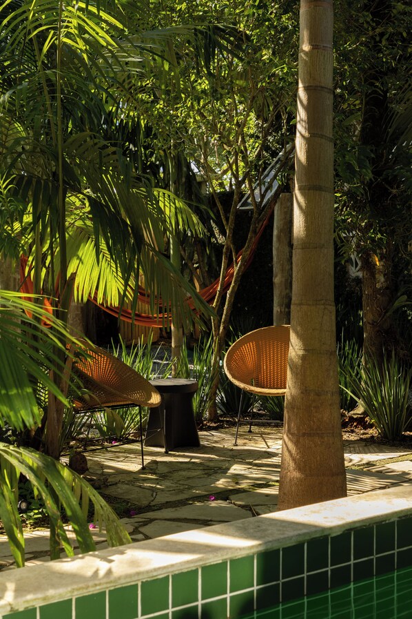 A tropical garden with a hammock, wicker chairs, and a tiled pool area. - O Portalzinho (Paraty)