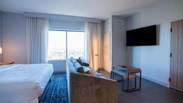A modern hotel room with a large bed, a sofa, a desk, and a TV mounted on the wall.