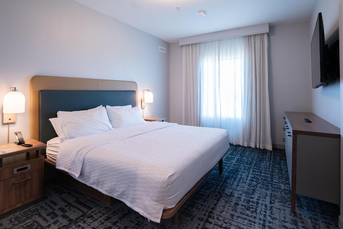 Une chambre d’hôtel équipée d’un lit, de tables de chevet, d’un bureau, d’une télévision et d’une fenêtre avec des rideaux.
