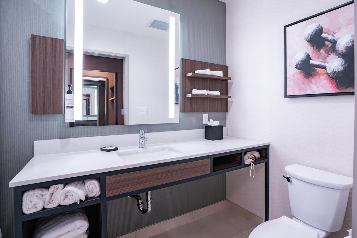 Un baño moderno con un espejo grande, lavabo blanco, espacio para toallas y un inodoro.