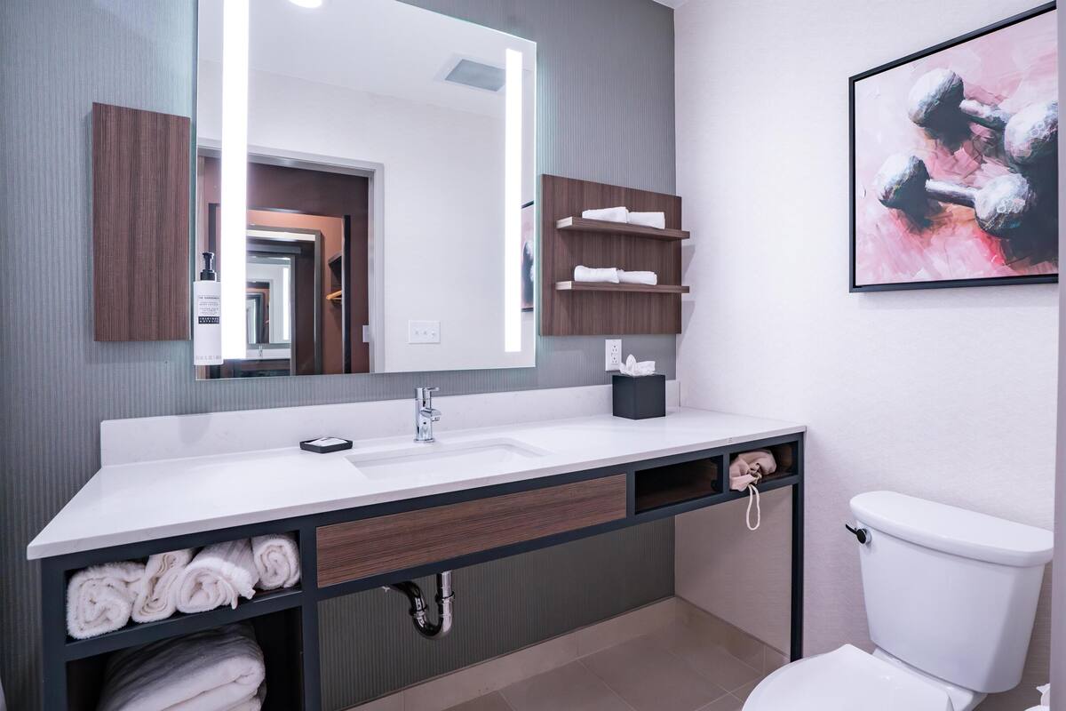 A modern bathroom with a large mirror, white sink, towel storage, and a toilet.
