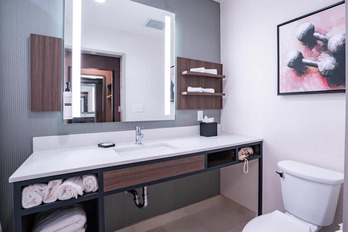 A modern bathroom with a large mirror, white sink, towel storage, and a toilet.