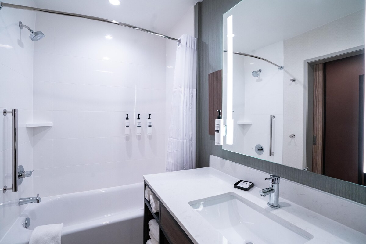 A modern bathroom with a bathtub, a large mirror, and a vanity with a sink.