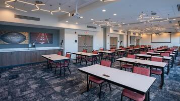 A conference room with tables and chairs, a projector screen, and a large wall art piece.