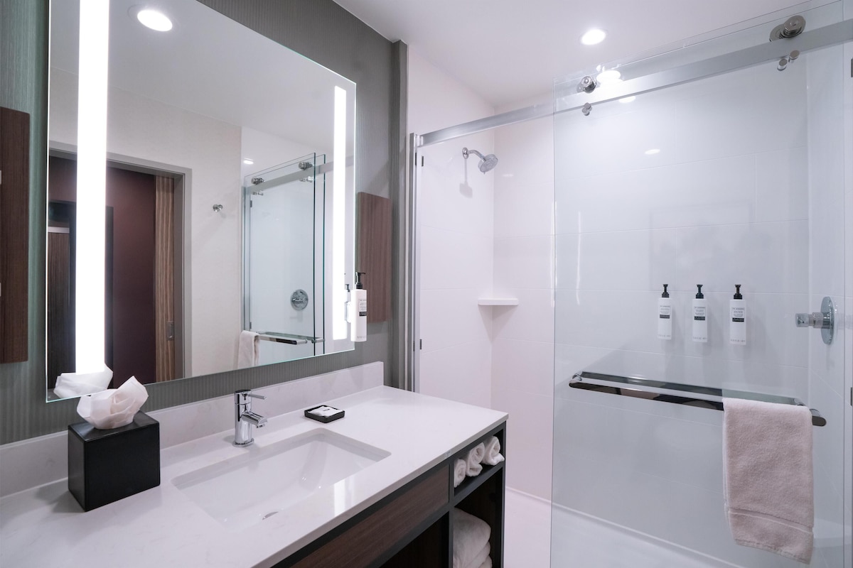 A modern bathroom with a large mirror, a white sink, and a glass-enclosed shower.