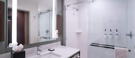 Un baño moderno con un espejo grande, un lavabo blanco y una ducha con mampara de vidrio.