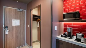 A hotel corridor with a wooden door, an evacuation plan sign, a coat rack, and a microwave on a red brick wall. - Hilton Garden Inn Hoover Birmingham (Birmingham)
