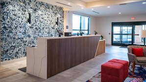 A reception area with a marble wall, a wooden reception desk, a red chair, and a large window. - Hilton Garden Inn Hoover Birmingham (Birmingham)
