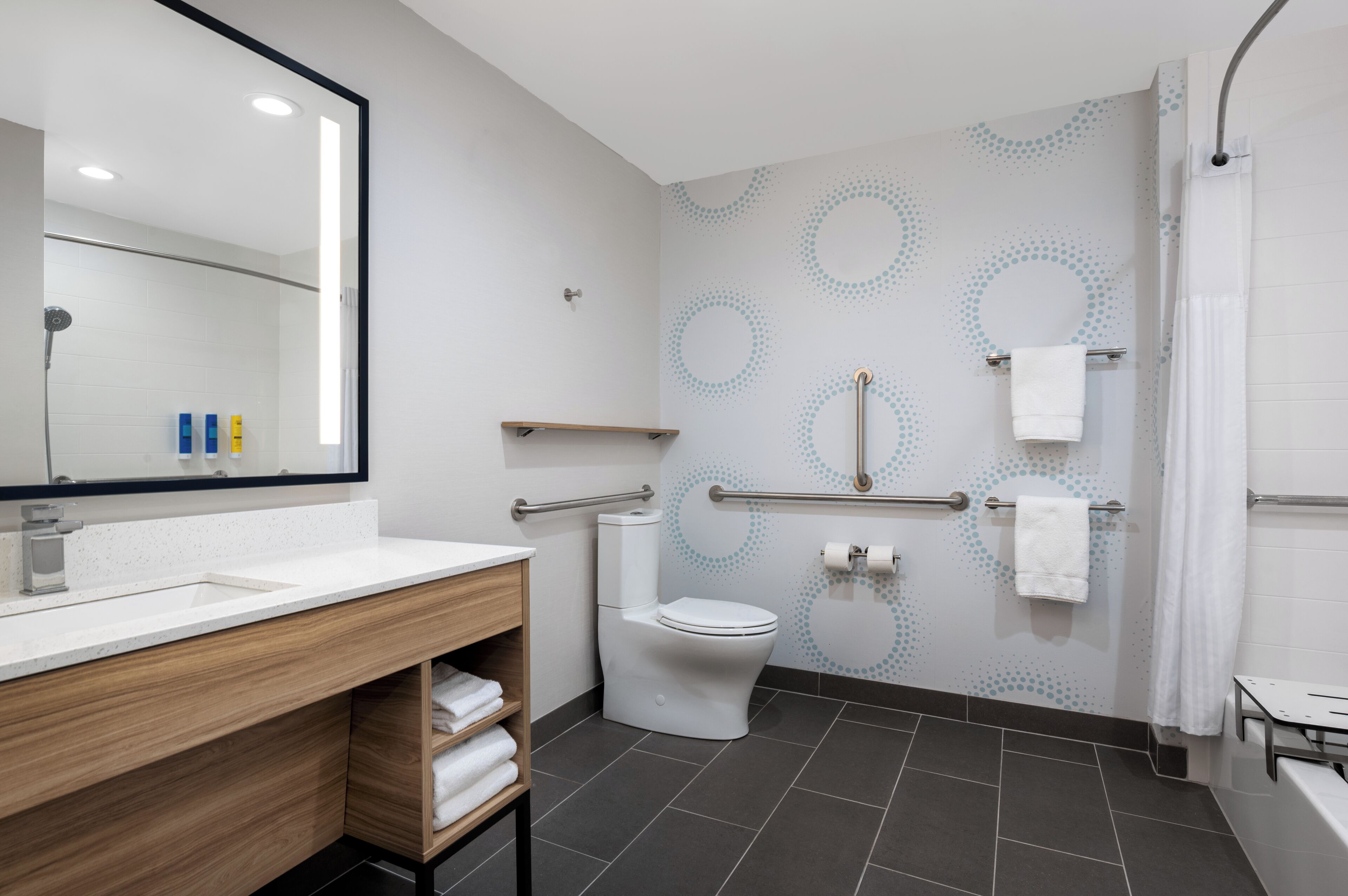 A modern bathroom with a white sink, wooden vanity, a toilet, and a shower area.