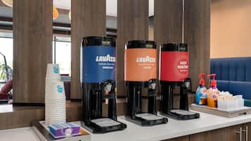 Un espace dédié au café, équipé de quatre distributeurs portant les inscriptions « Lavazza » et « EAU CHAUDE », situé dans un hôtel.