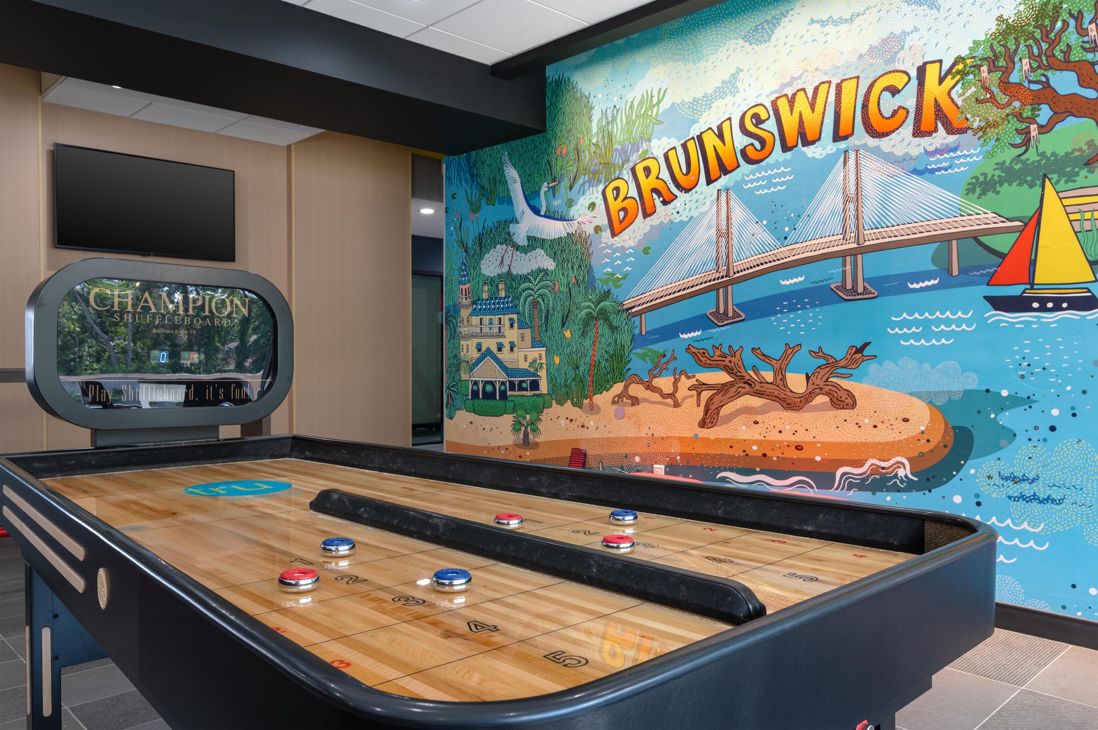 A shuffleboard table with a mural of a bridge and sailboat in the background.