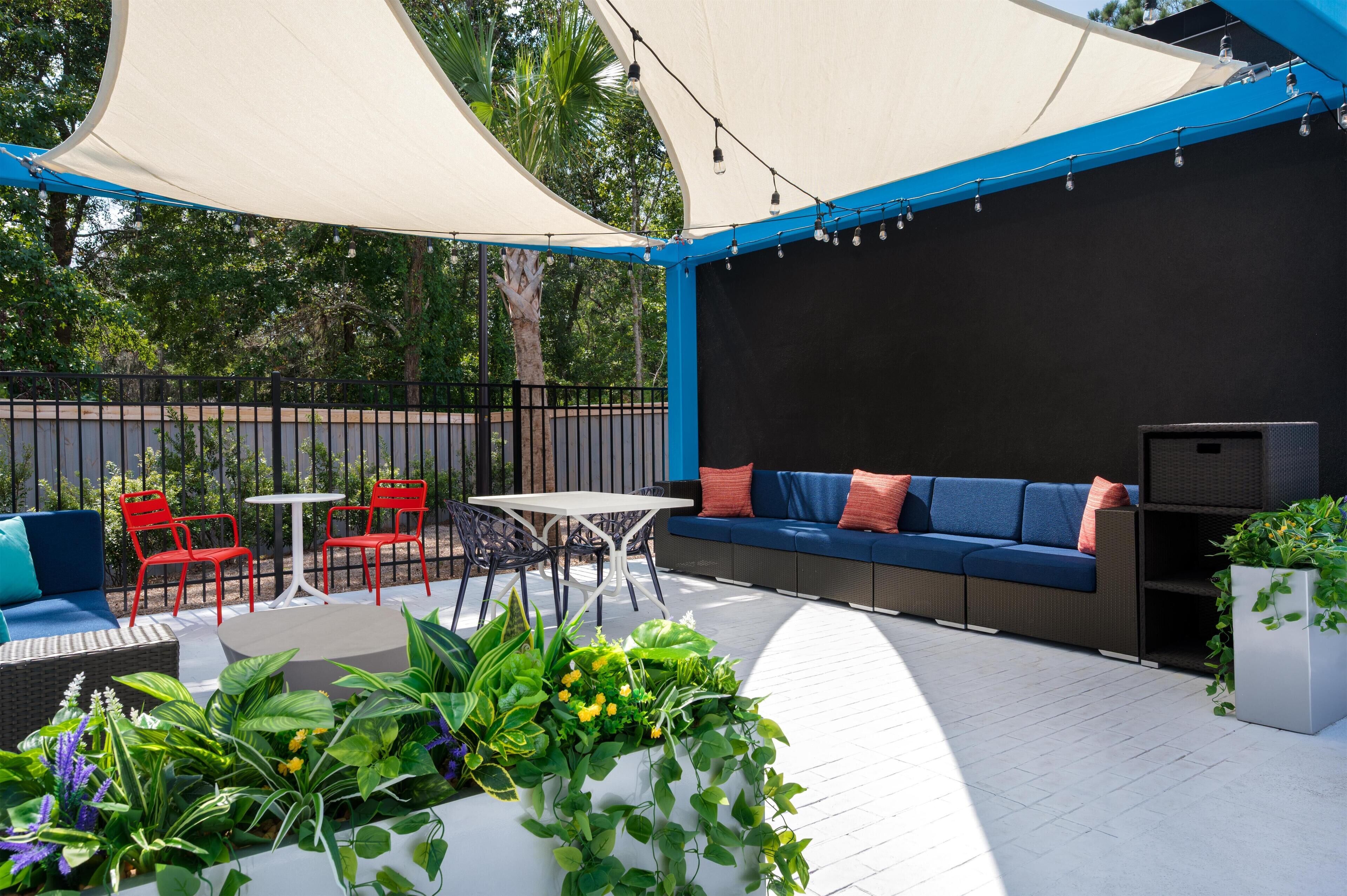 An outdoor patio area with a white table, red chairs, a blue sofa, and a variety of potted plants.