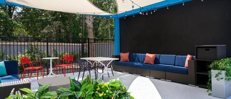 An outdoor patio area with a white table, red chairs, a blue sofa, and a variety of potted plants.