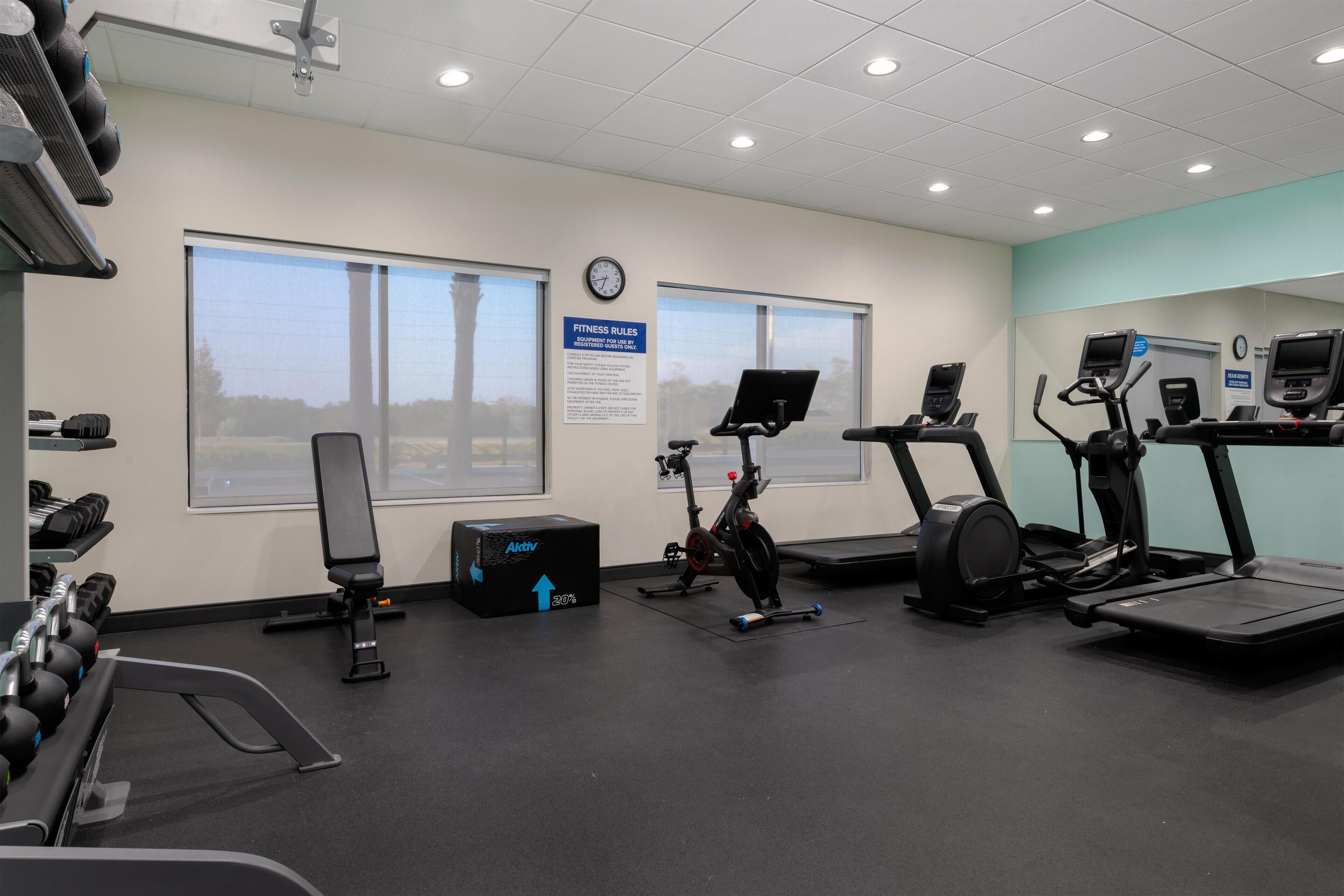 A gym with treadmills, an elliptical, a bench, and dumbbells.