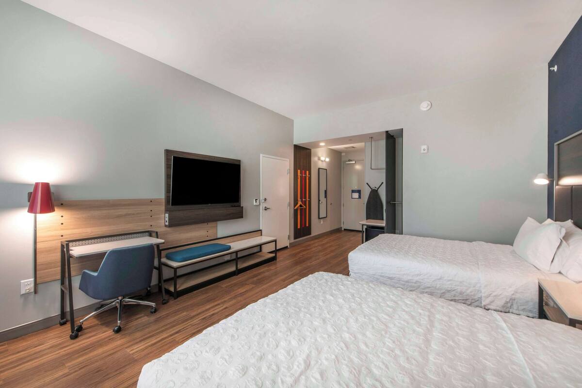 Una habitación de hotel con una cama, un escritorio con una silla, un televisor y una lámpara roja.