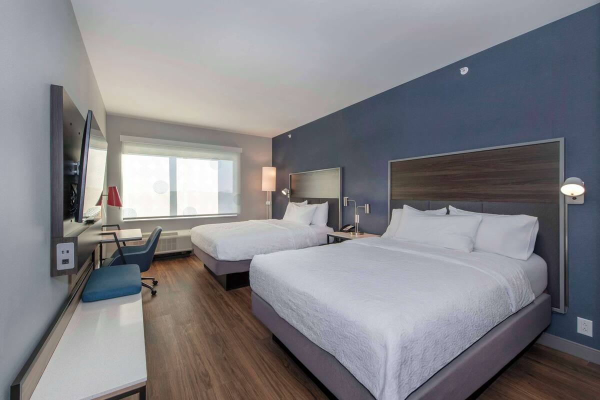 Habitación de hotel con dos camas, un escritorio, una silla, un televisor y una ventana con vistas.