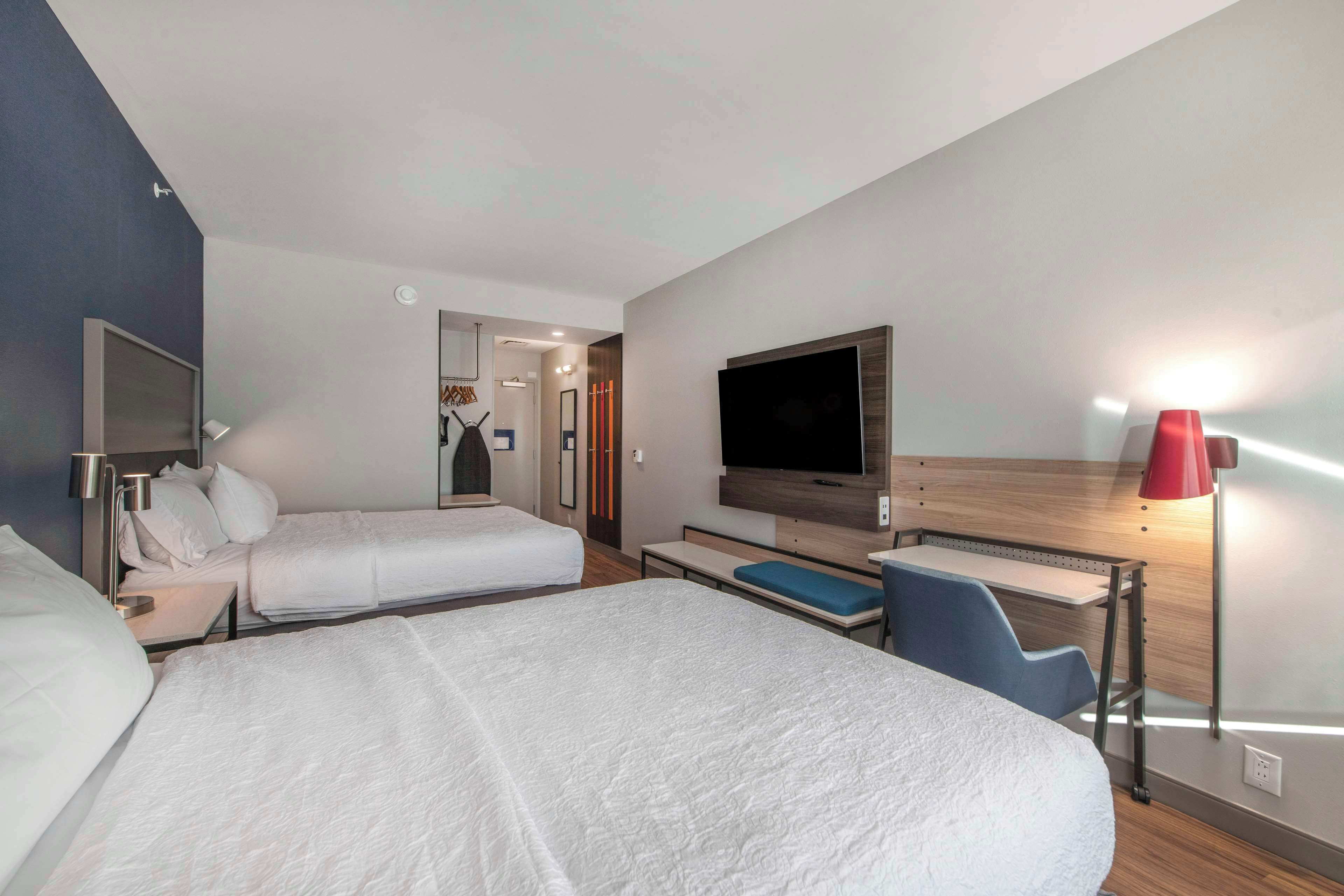 A hotel room with two beds, a TV, a desk, and a red lamp.