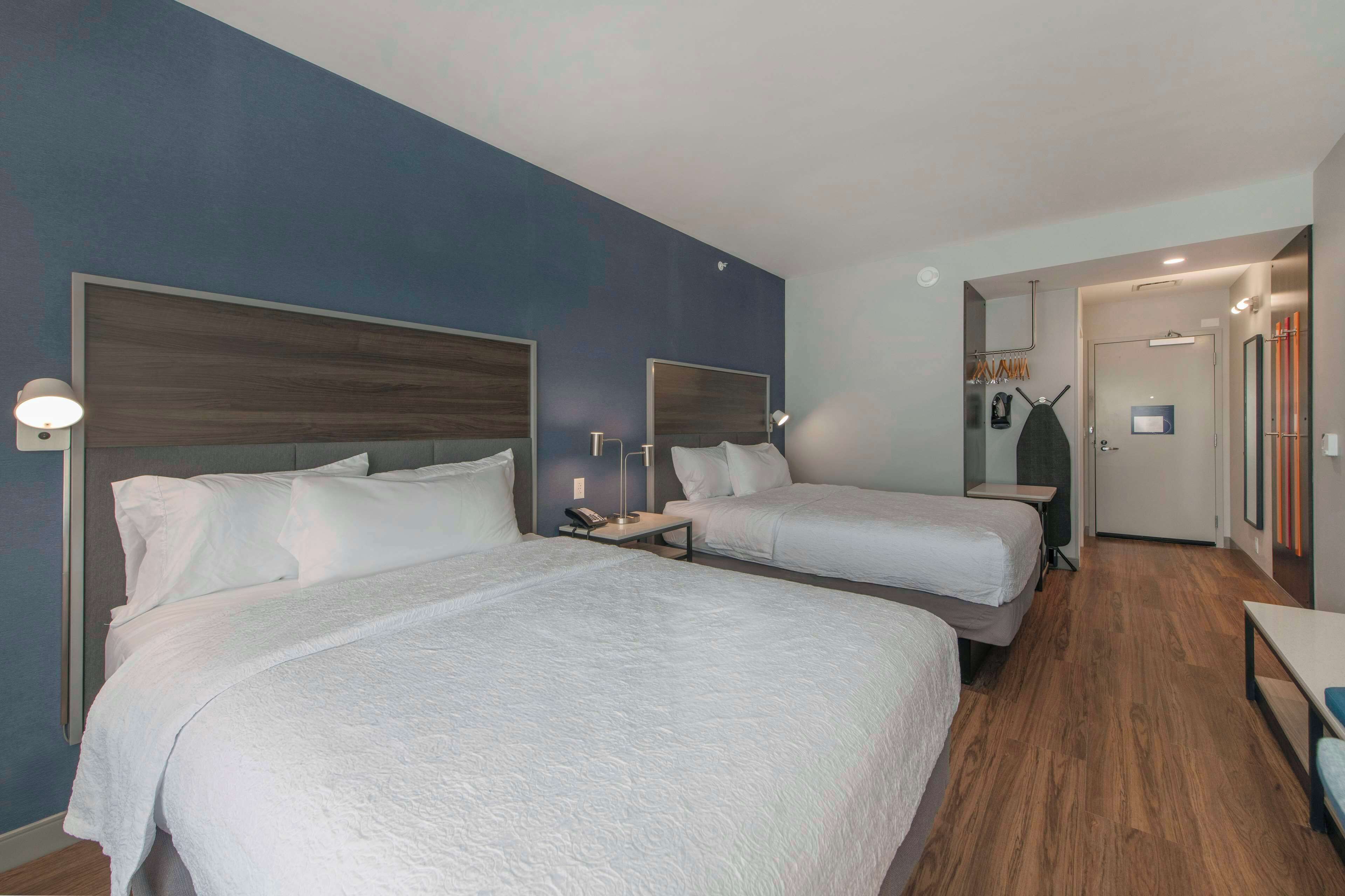 A hotel room with two beds, a small table, and a nightstand with a phone.