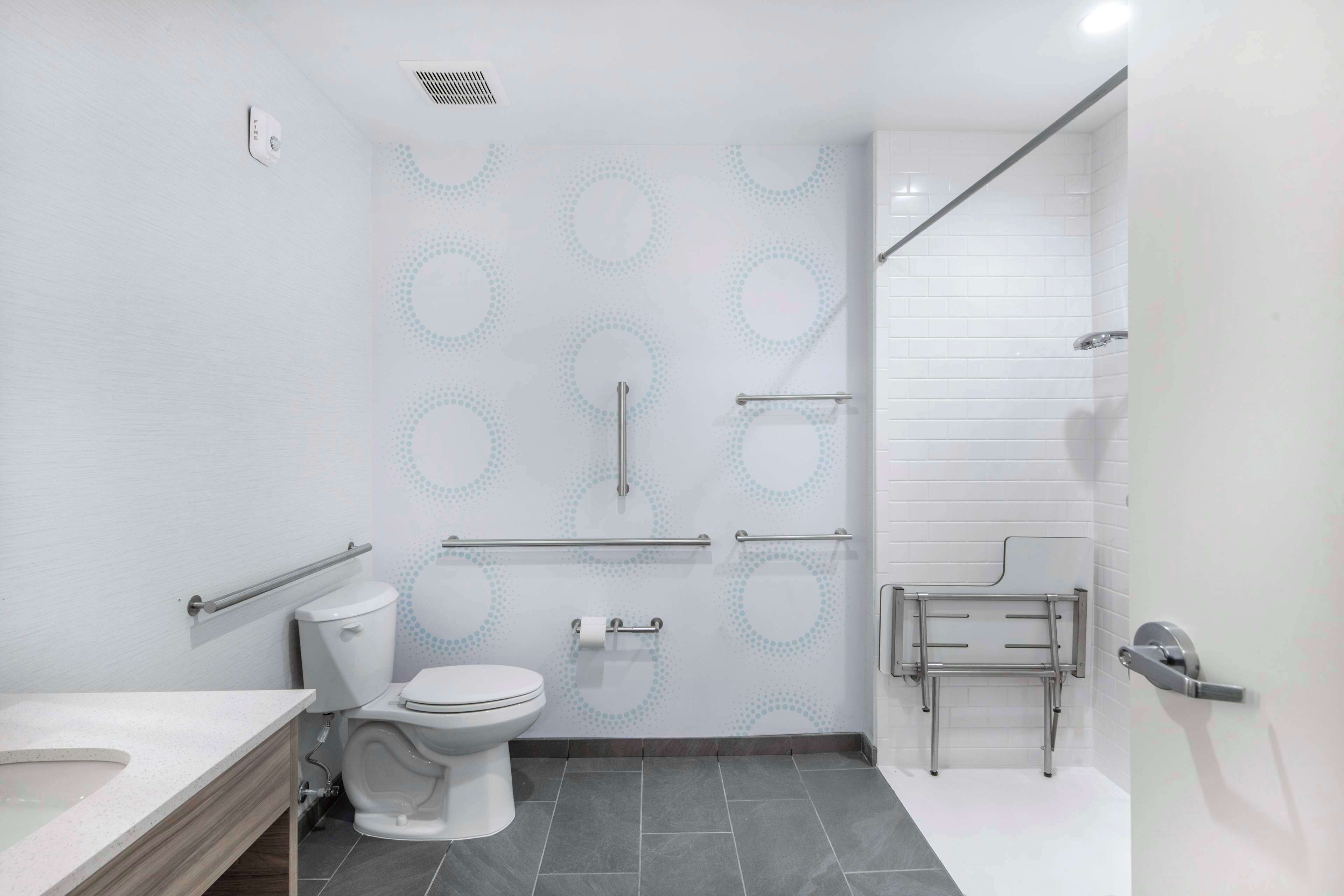 Een moderne badkamer met toilet, bidet en douche, voorzien van handgrepen en een handrail.