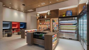 Un espacio comercial moderno con un mostrador central, estantes llenos de aperitivos y un expositor refrigerado.