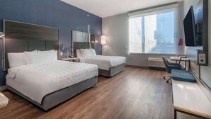 Habitación de hotel con dos camas, un escritorio, una silla, un televisor y un ventanal grande.