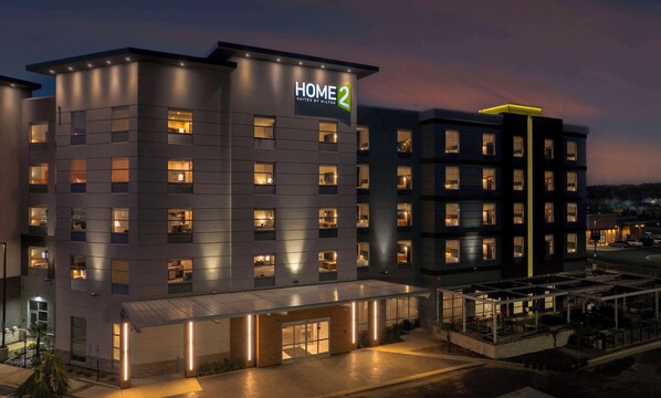 A modern hotel with a "HOME 2" sign, multiple floors, and a covered outdoor area with seating. - Home2 Suites By Hilton Lumberton (Lumberton)