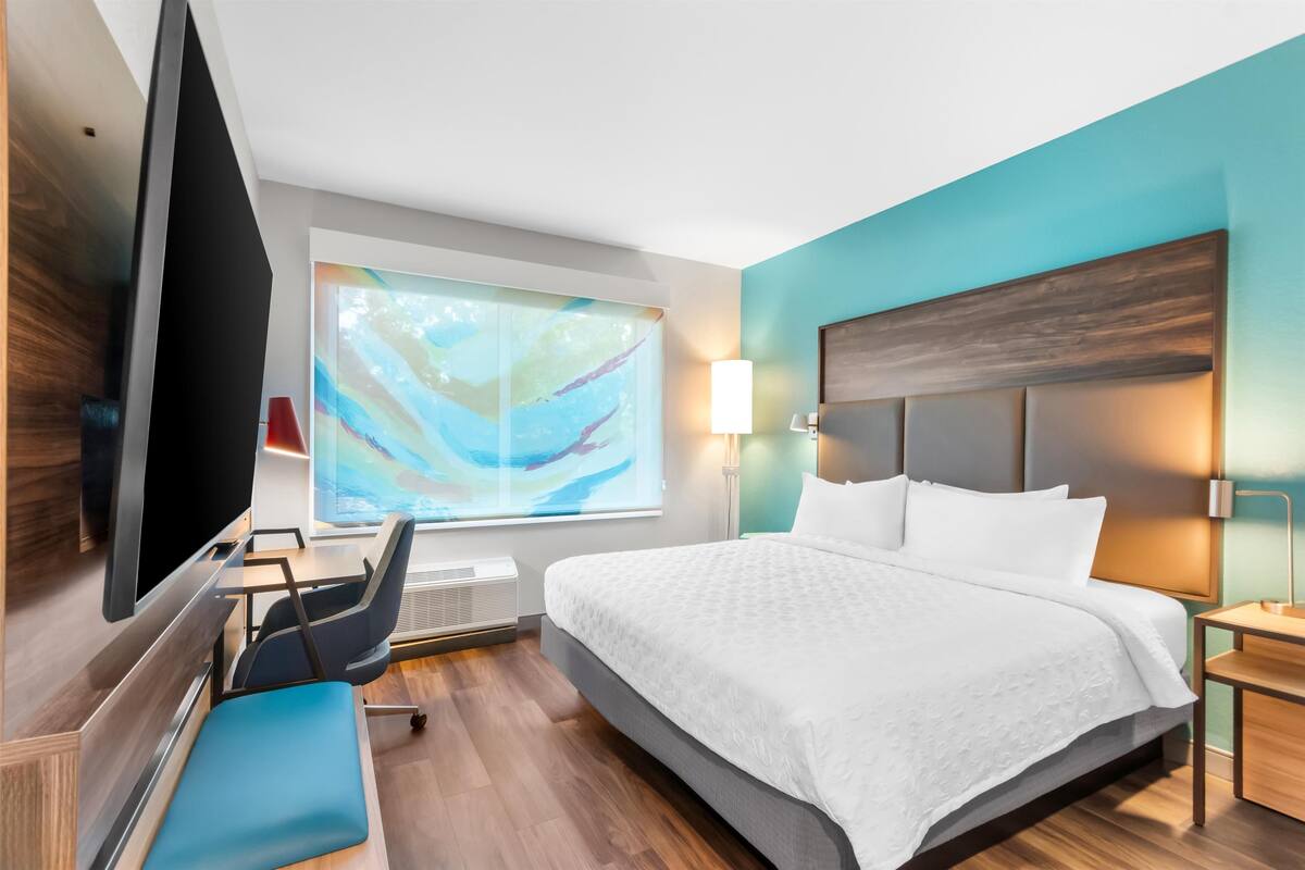 Quarto de hotel moderno com uma cama grande, uma escrivaninha, uma cadeira e uma televisão.