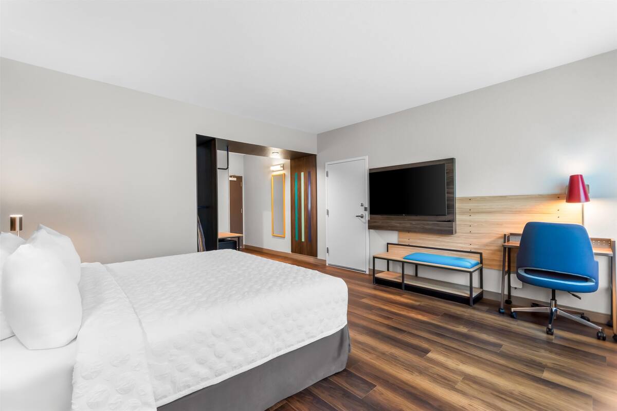 Quarto de hotel com cama, escrivaninha, cadeira, televisão e abajur vermelho.