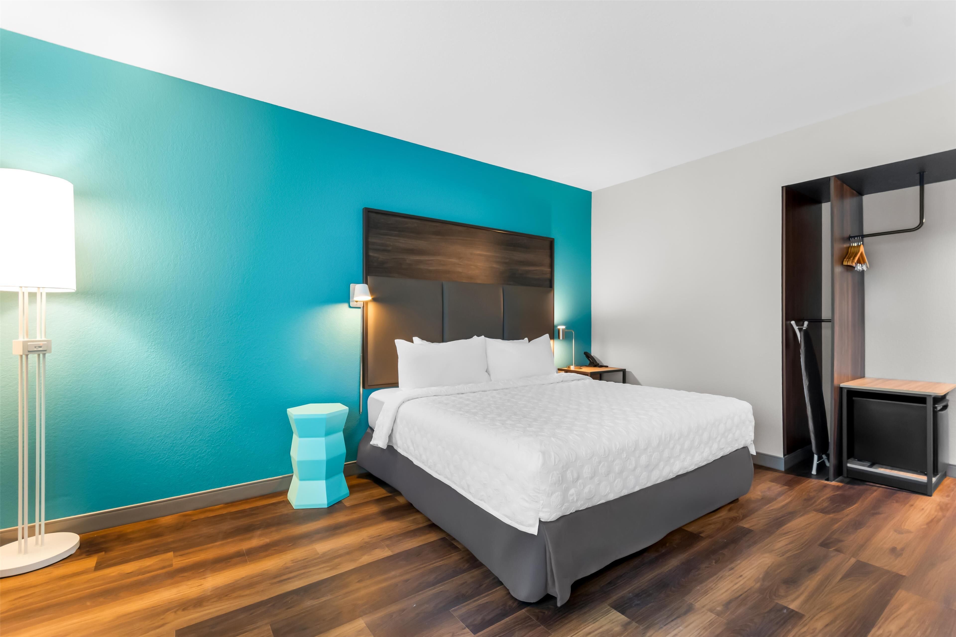 A modern hotel room with a large bed, a nightstand, a lamp, and a wardrobe.
