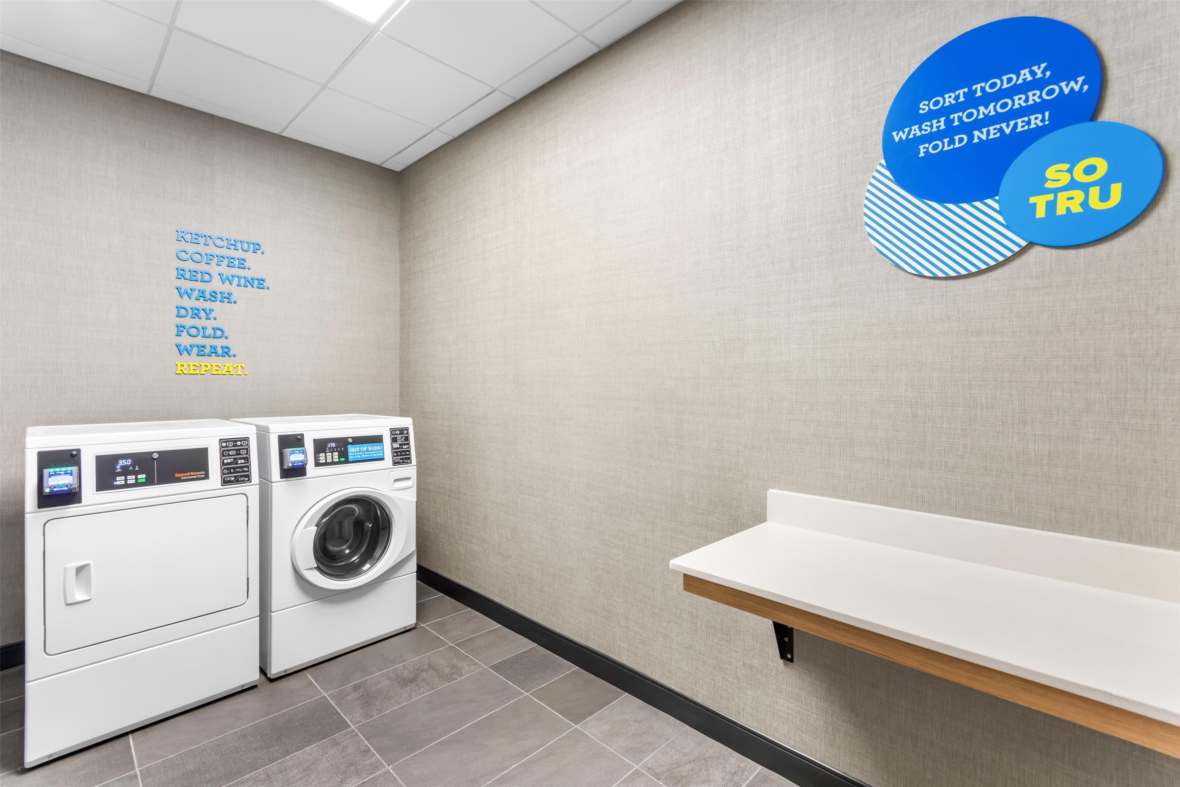 A laundry room with two front-loading washing machines, a white shelf, and motivational wall decals.