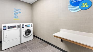 A laundry room with two front-loading washing machines, a white shelf, and motivational wall decals.