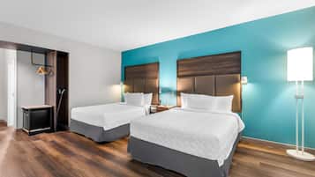 Una habitación de hotel con dos camas, un escritorio, una silla, una lámpara y un armario.