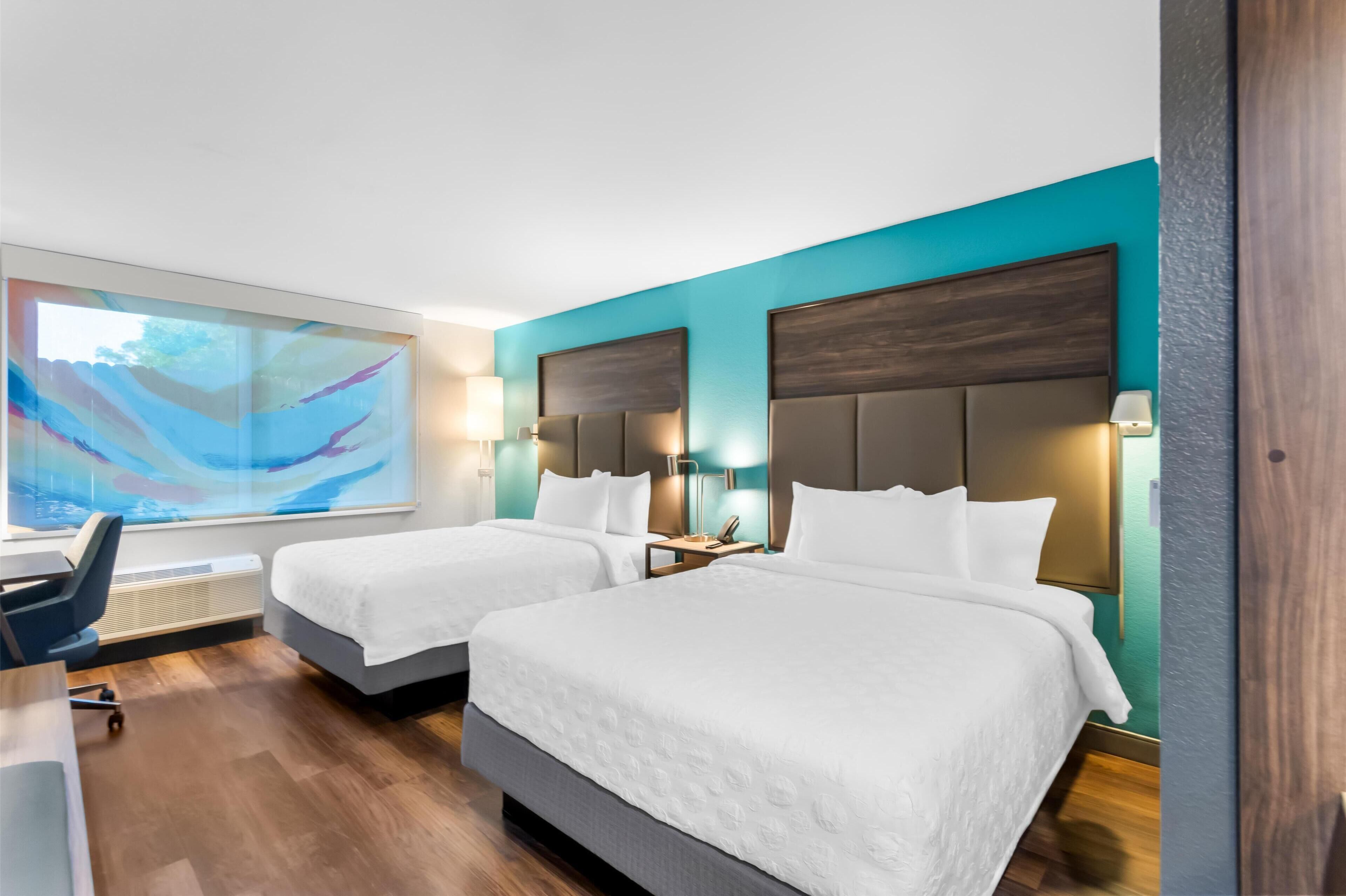 Habitación de hotel con dos camas, un escritorio y un cuadro abstracto grande en la pared.