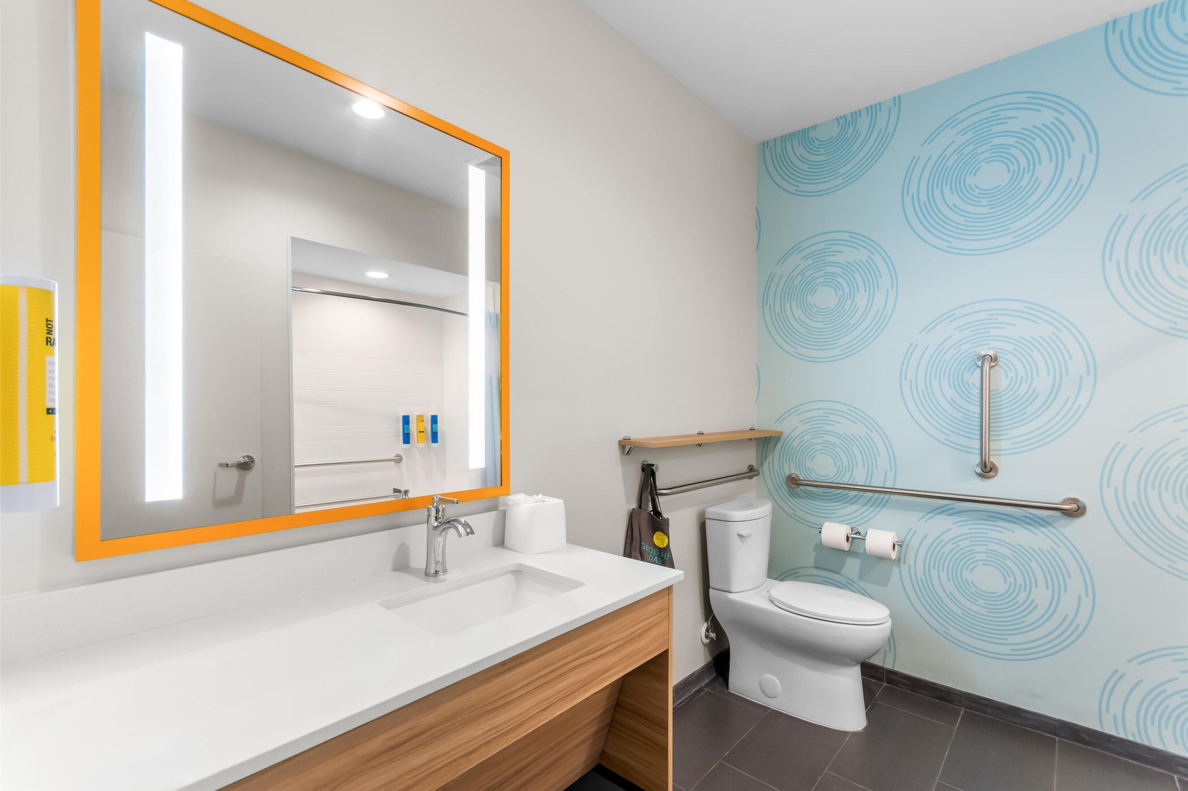A modern bathroom with a large mirror, white sink, and a toilet.